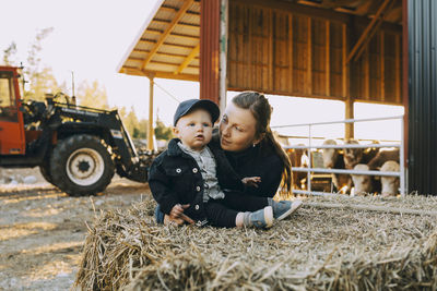 Mother looking at son sitting on hay bale in farm