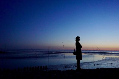 Silhouette woman standing on beach against clear sky during sunset