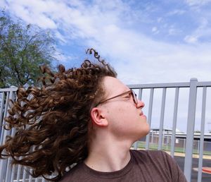 Portrait of teenage boy with curly hair against railing against sky