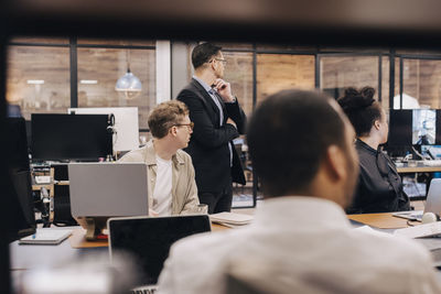 Business manager and colleagues looking at computer monitor during meeting in office