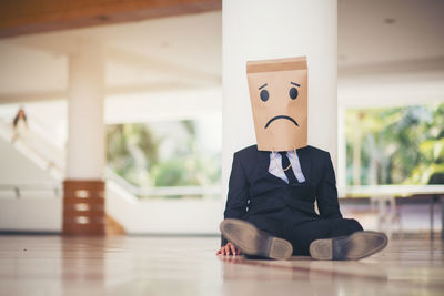 Businessman wearing paper bag of sad face while sitting on floor