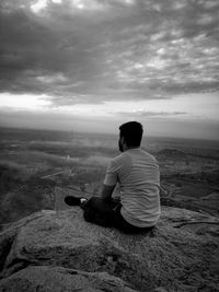 Rear view of man sitting on land against sky