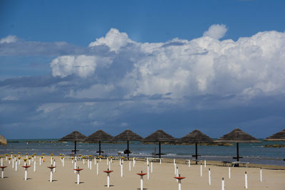 Parasols on shore at beach against cloudy sky