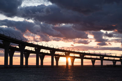 Silhouette bridge over sea against sky during sunset