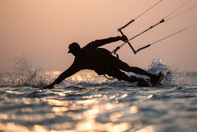 Silhouette man kitesurfing on sea against clear sky at sunset