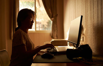 A woman working on a computer in a room filled with warm morning light