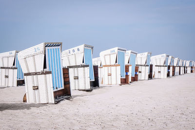 Hooded chairs at sandy beach against clear sky