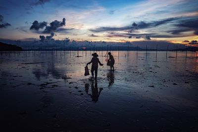 Silhouette people on beach against sky during sunset