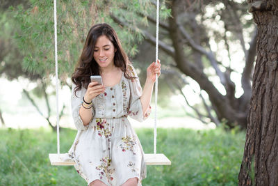 Happy young woman using phone while standing on plants