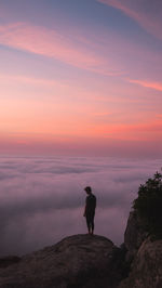 Man standing on rock against sky during sunset