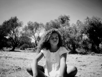 Girl sitting with eyes closed on field against sky