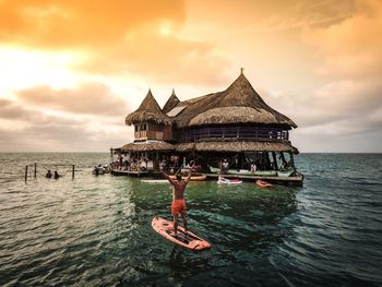 Rear view of man standing on paddleboard in sea against sky