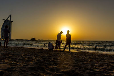 People at beach against sky during sunset