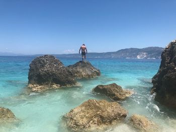 Shirtless man standing on rock in sea against blue sky