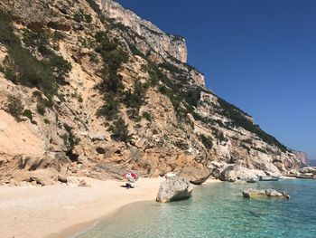 Man on cliff by sea against clear blue sky