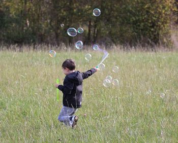 Playful boy blowing bubbles while running on grass