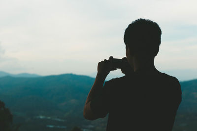 Rear view of silhouette man photographing while standing against sky