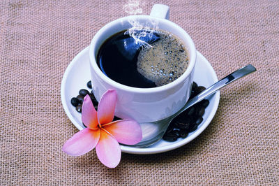 High angle view of black coffee with frangipani coffee beans on table