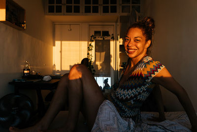 Portrait of a smiling young woman sitting on a bed in a bedroom