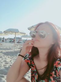 Portrait of young woman in sunglasses at beach against clear sky