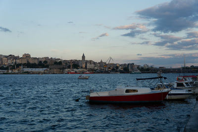 Sailboats moored on sea by buildings against sky during sunset