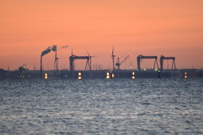 Commercial dock by sea against orange sky