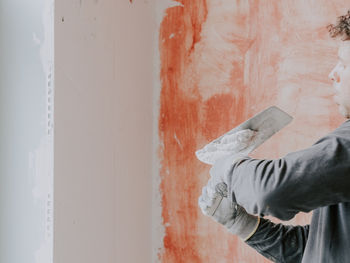 A young guy puts putty on a spatula against the background of prepared walls with red mortar