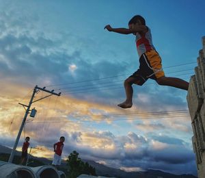 Low angle view of boy jumping against sky during sunset