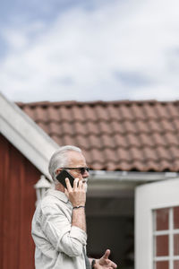 Midsection of man photographing by building against sky