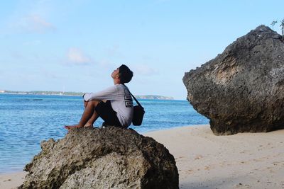 Man sitting on rock by sea against sky