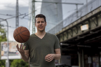 Portrait of young man with basketball standing outdoors