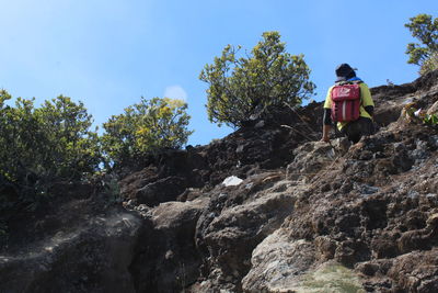 Low angle view of man standing on rock against sky