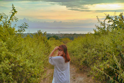 Woman standing by plants against sky during sunset