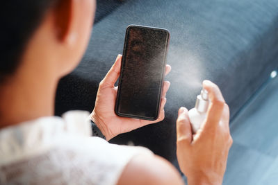 Midsection of woman spraying sanitizer on smart phone