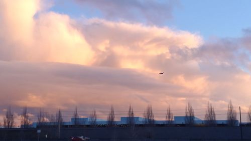 Airplane flying over city against sky during sunset