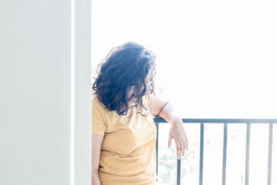Woman looking away while standing against window at home