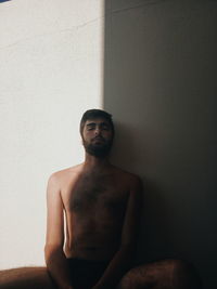 Portrait of young man sitting against wall