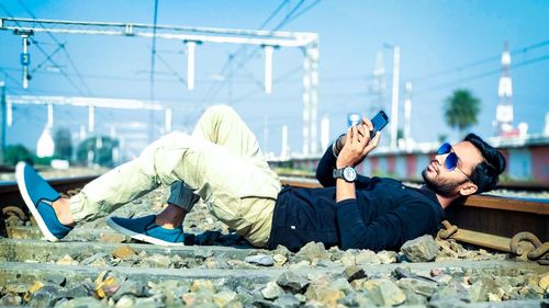 Young man using phone while lying on railroad track