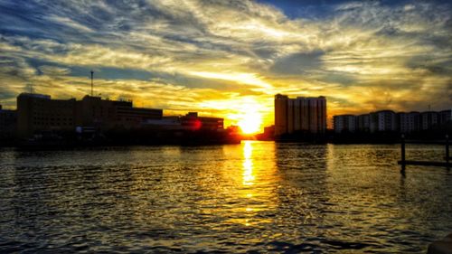 City buildings by sea against sky during sunset