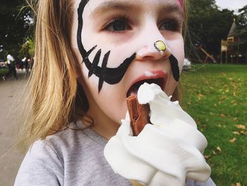 Close-up of girl with face paint eating ice cream at park