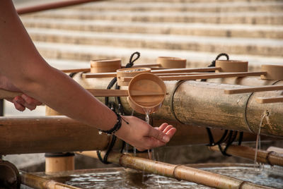 Cropped hands holding bamboo dipper at fountain