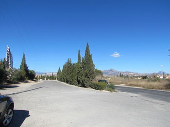 Road by trees against blue sky