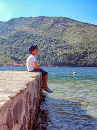 Side view of boy sitting on pier by lake
