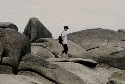 Side view of man walking on rock against sky