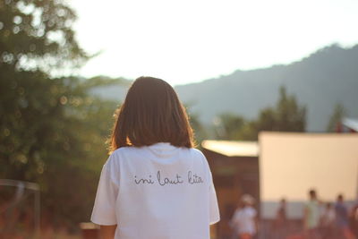 Rear view of woman wearing t-shirt with text against trees