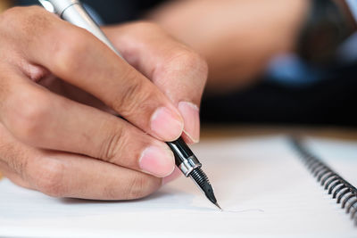 Midsection of person holding paper with pen on table