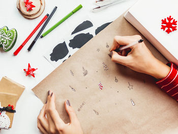 Woman draws new year symbols on craft paper. festive flat lay background. diy gifts for holidays.