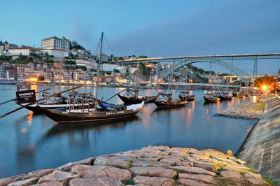 Boats on douro river by dom luis i bridge in city at dusk