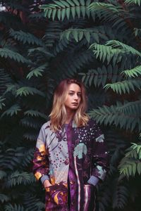 Portrait of young woman with hands in pockets standing amidst trees