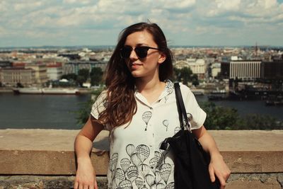 Young woman wearing sunglasses standing against cityscape in city